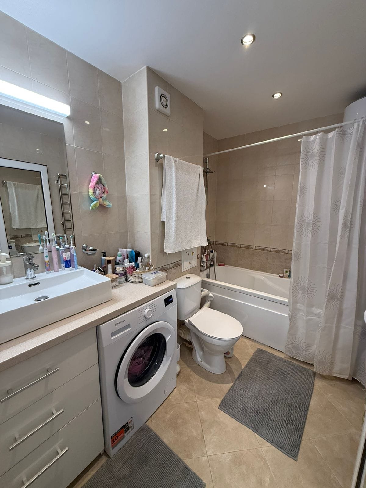 Современная ванная комната с ванной, туалетом, стиральной машиной и зеркалом, оформленная в светлых тонах.