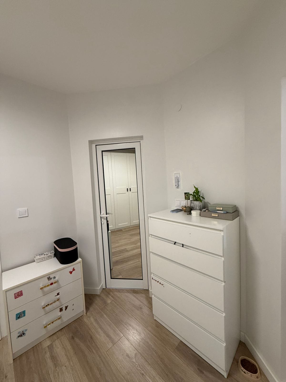 Двухкомнатный апартамент с белыми стенами, светлым полом, зеркалом и комодом, оформленным в современном стиле.