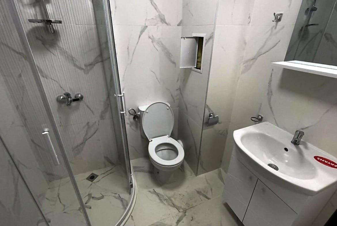 Современная ванная комната с душевой кабиной, унитазом и раковиной, оформленная в светлых тонах, идеальна для покупки недвижимости в Болгарии.