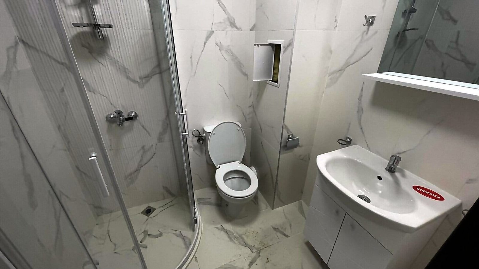 Современная ванная комната с душевой кабиной, унитазом и раковиной, оформленная в светлых тонах, идеальна для покупки недвижимости в Болгарии.