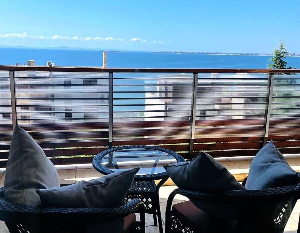 Уютный балкон с двумя креслами и стеклянным столиком, открывающий вид на море и синее небо в Болгарии.