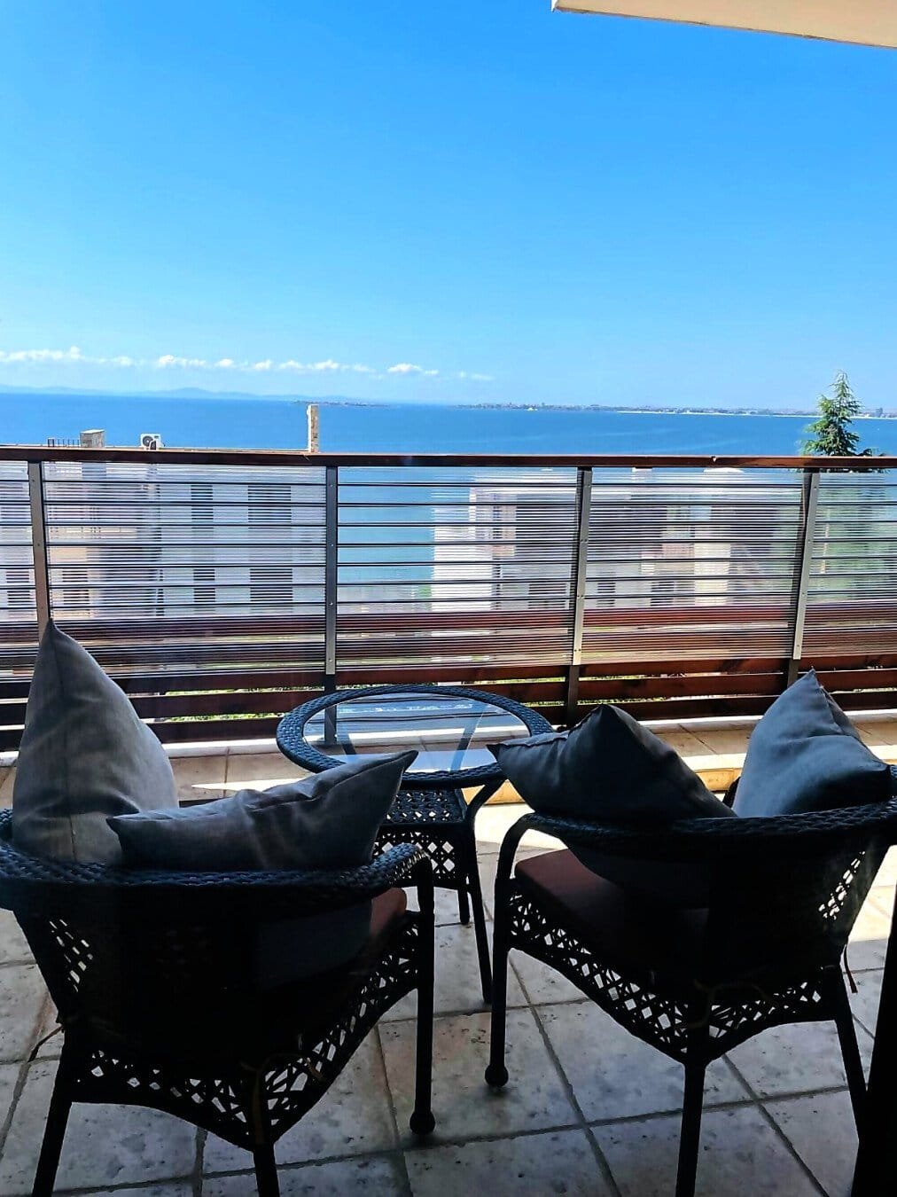 Уютный балкон с двумя креслами и стеклянным столиком, открывающий вид на море и синее небо в Болгарии.