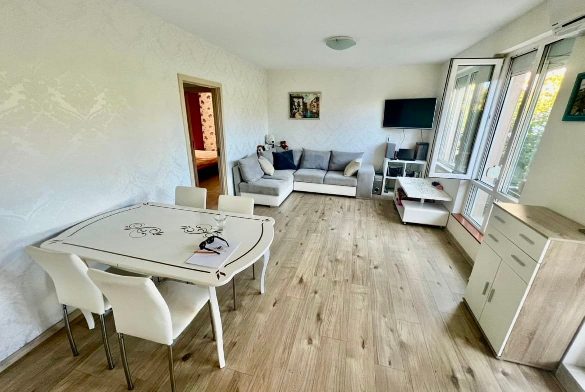 Современная квартира в Болгарии с просторной гостиной, обеденным столом и большими окнами, наполненная естественным светом.