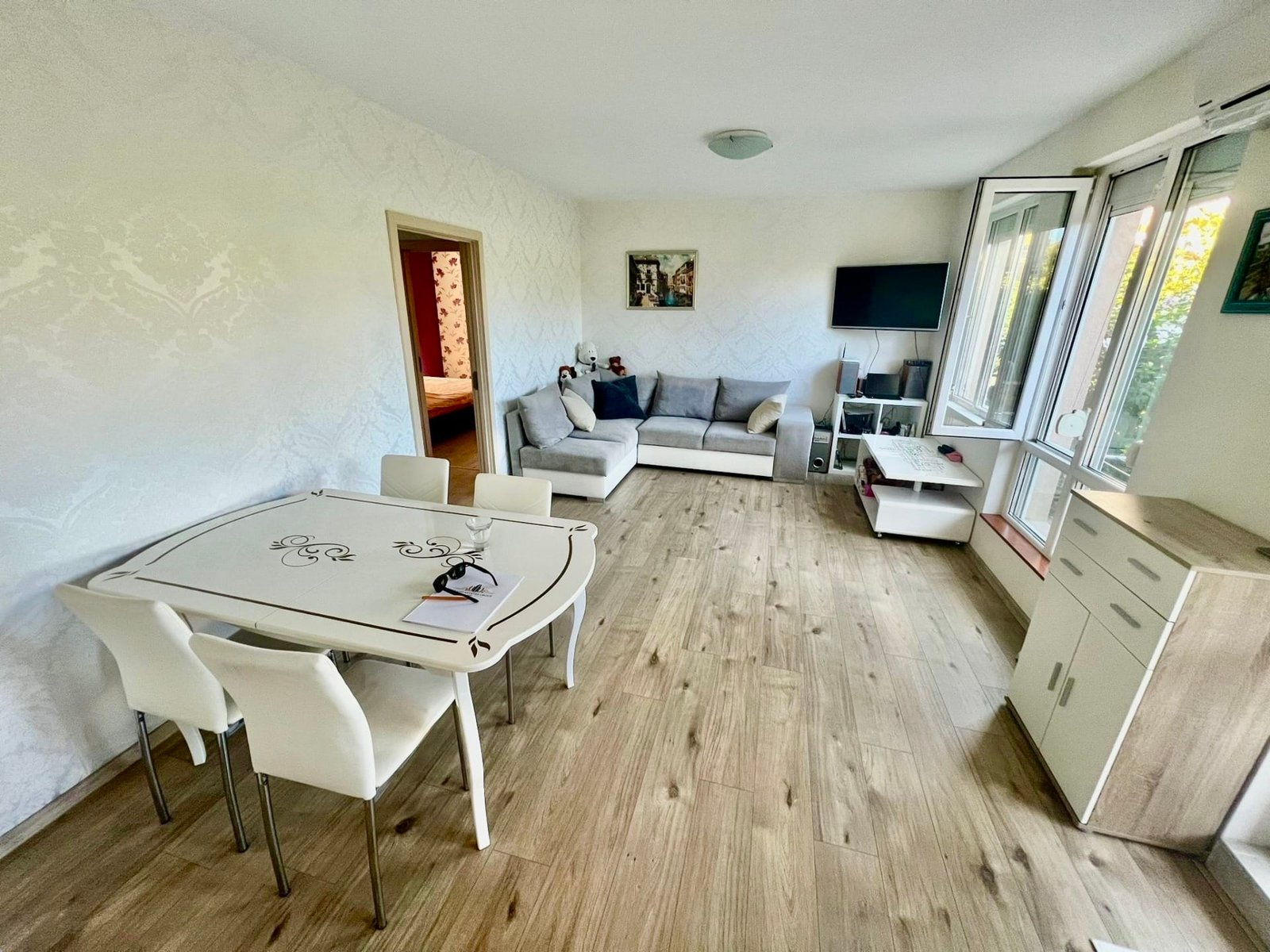 Современная квартира в Болгарии с просторной гостиной, обеденным столом и большими окнами, наполненная естественным светом.