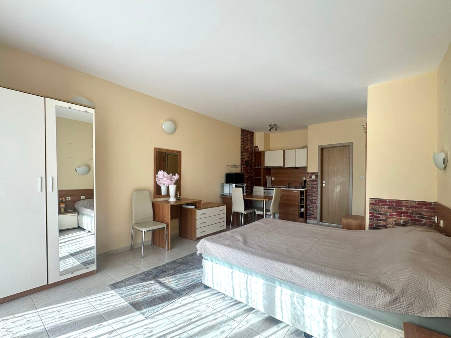 Компактная квартира-студия в Болгарии с кухней, обеденной зоной, дверью в ванную и светлыми тонами. Подходит для отдыха и жизни.