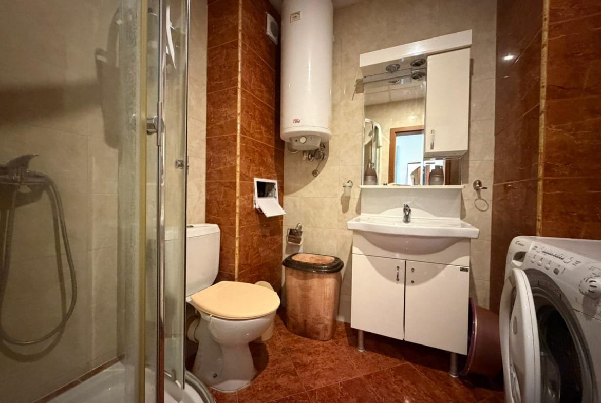 Современная ванная комната с душевым кабинетом, умывальником, унитазом и стиральной машиной в интерьере в теплых тонах.