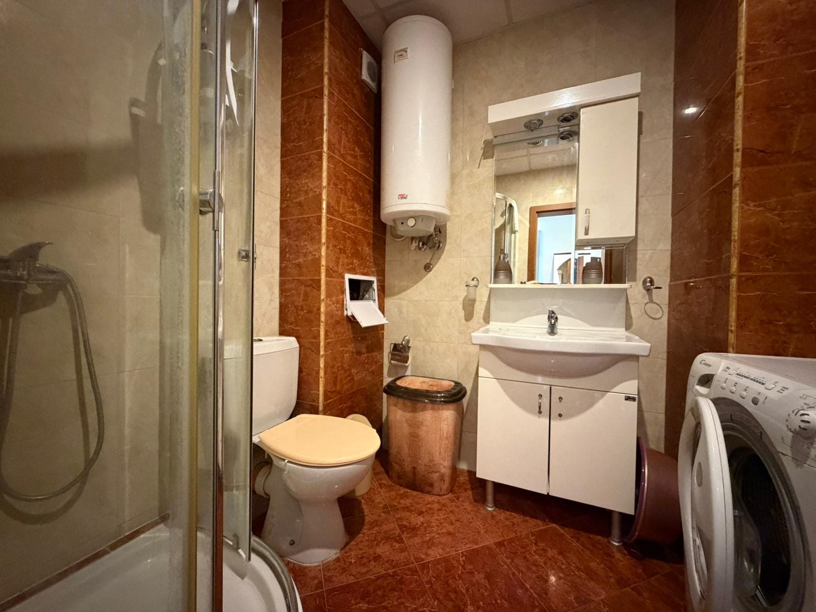 Современная ванная комната в квартире с душевой и стиральной машиной Современная ванная комната с душевым кабинетом, умывальником, унитазом и стиральной машиной в интерьере в теплых тонах.