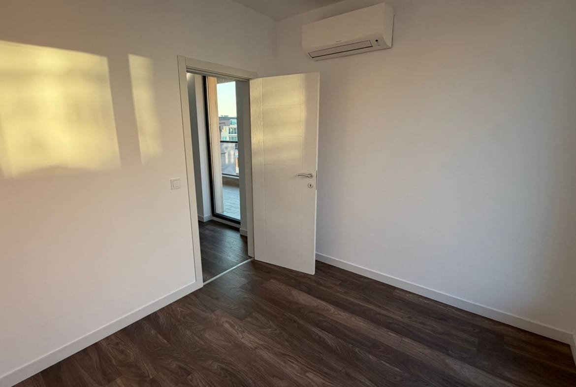 Современная комната с деревянным полом и балконными дверями, готовая для продажи недвижимости в Болгарии.