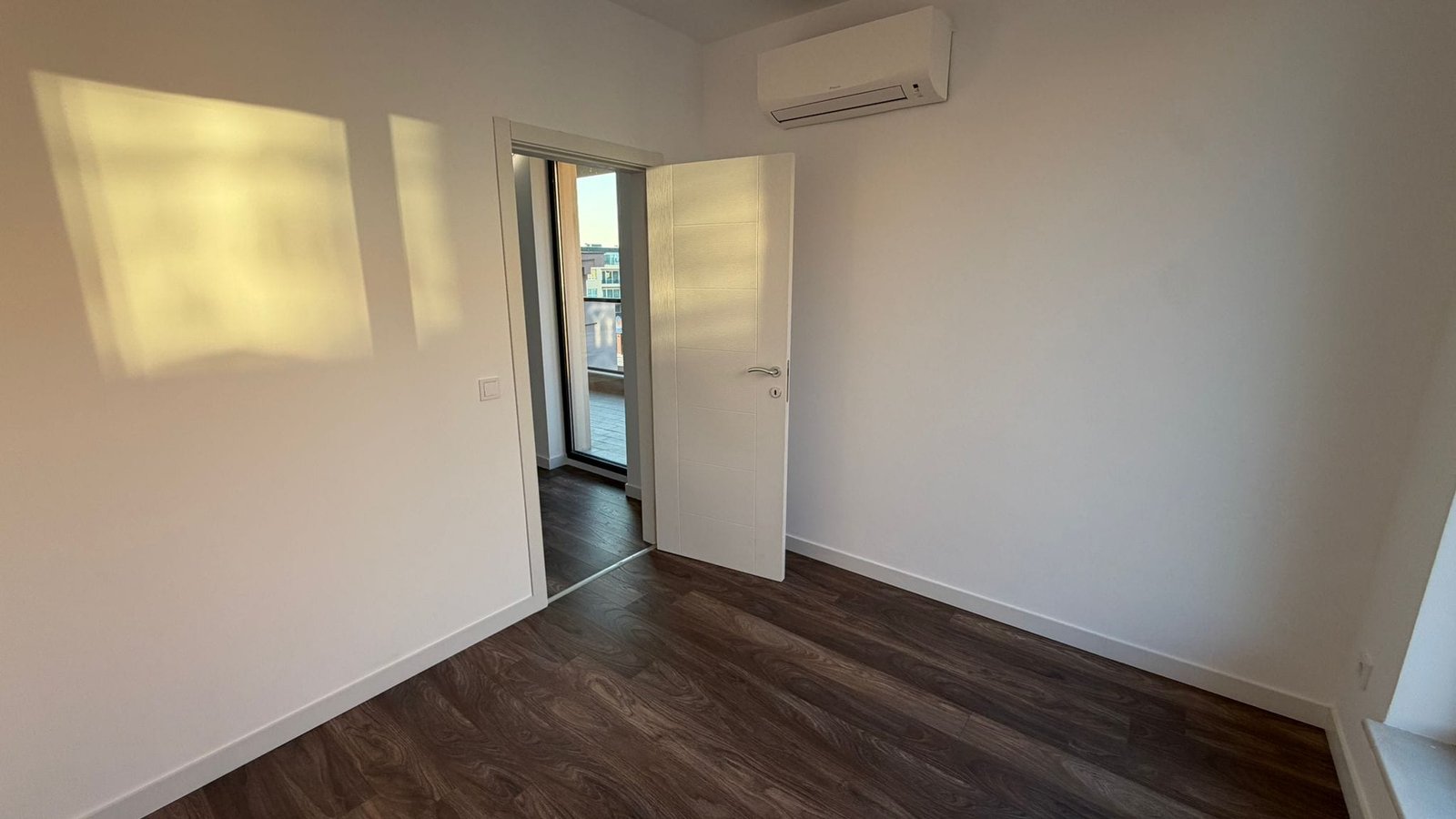 Современная спальня с балконной дверью и кондиционером Современная комната с деревянным полом и балконными дверями, готовая для продажи недвижимости в Болгарии.