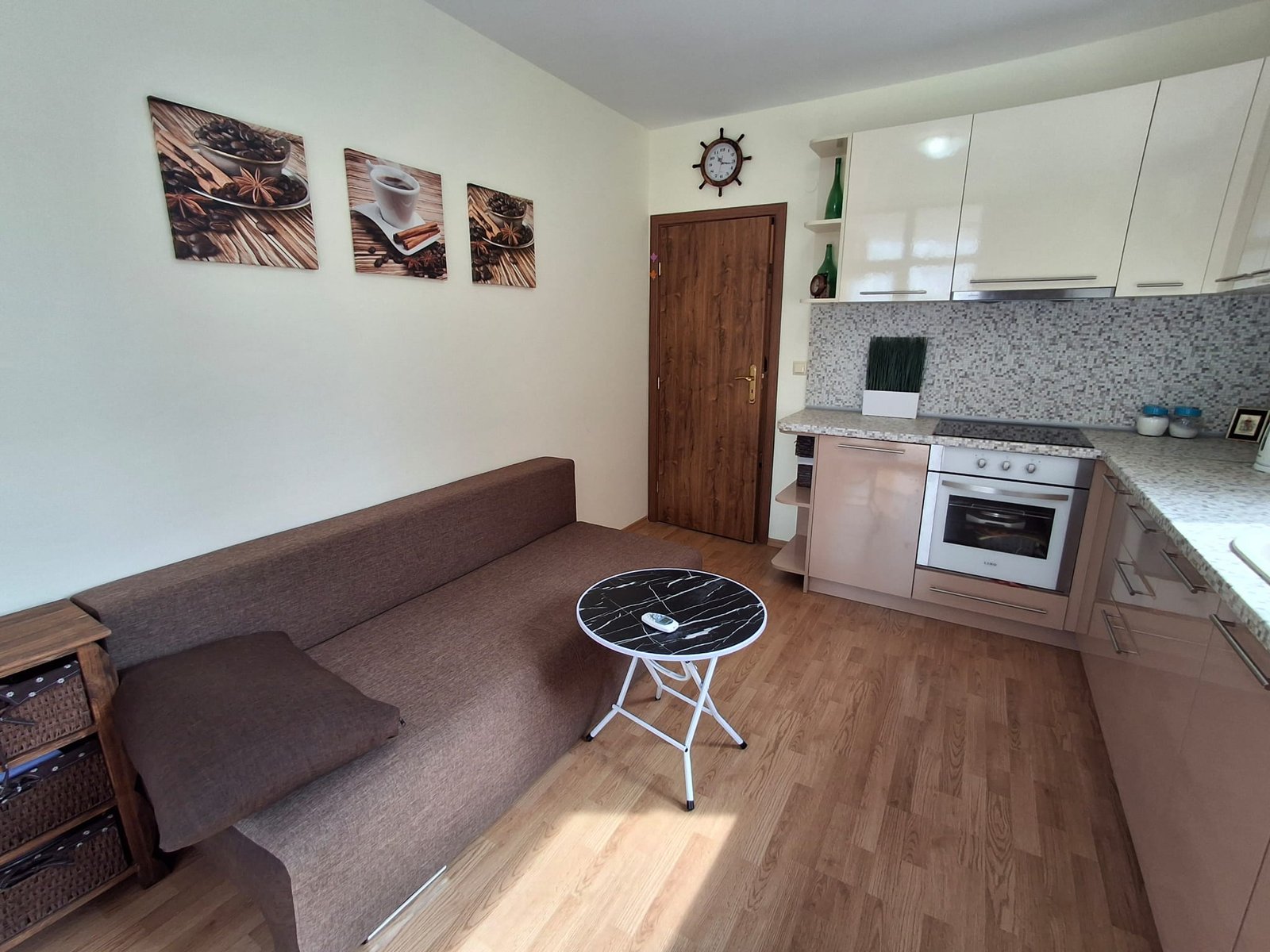 Современный интерьер квартиры с угловым диваном, журнальным столиком и кухонной зоной с плитой и темной столешницей.