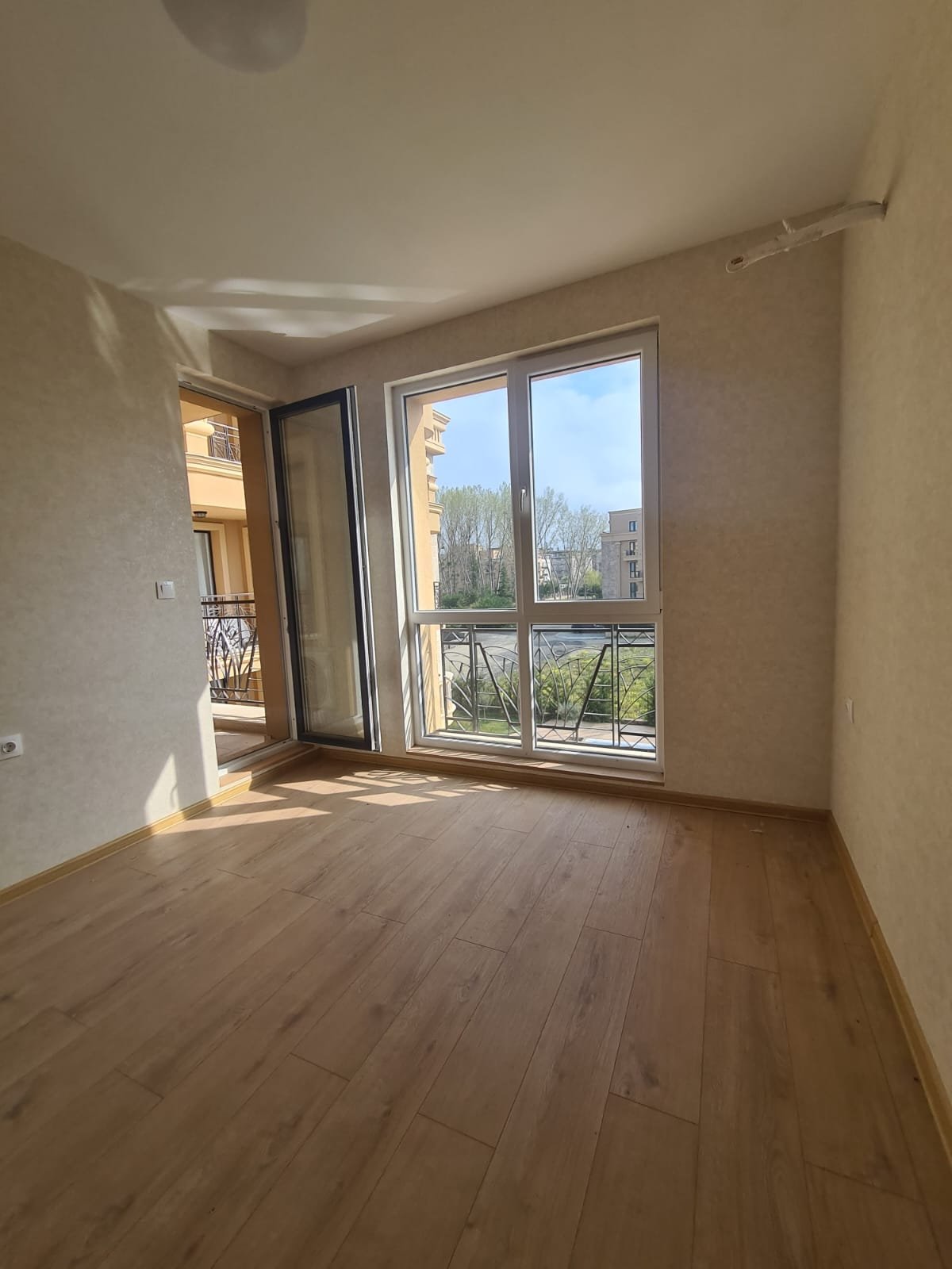 Светлая комната с большими окнами, выходящими на балкон, идеальна для покупки недвижимости в Болгарии.