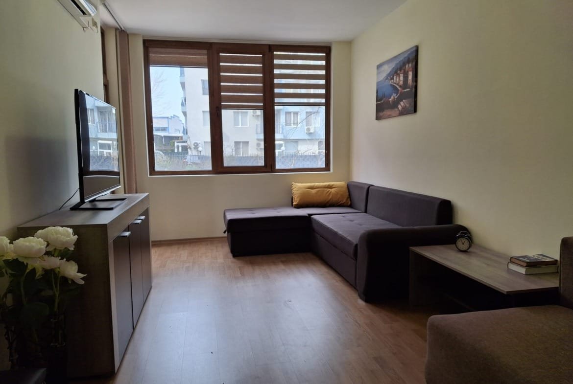 Современная гостиная с диваном, телевизором, столом и большим окном, оформленная в светлых тонах.