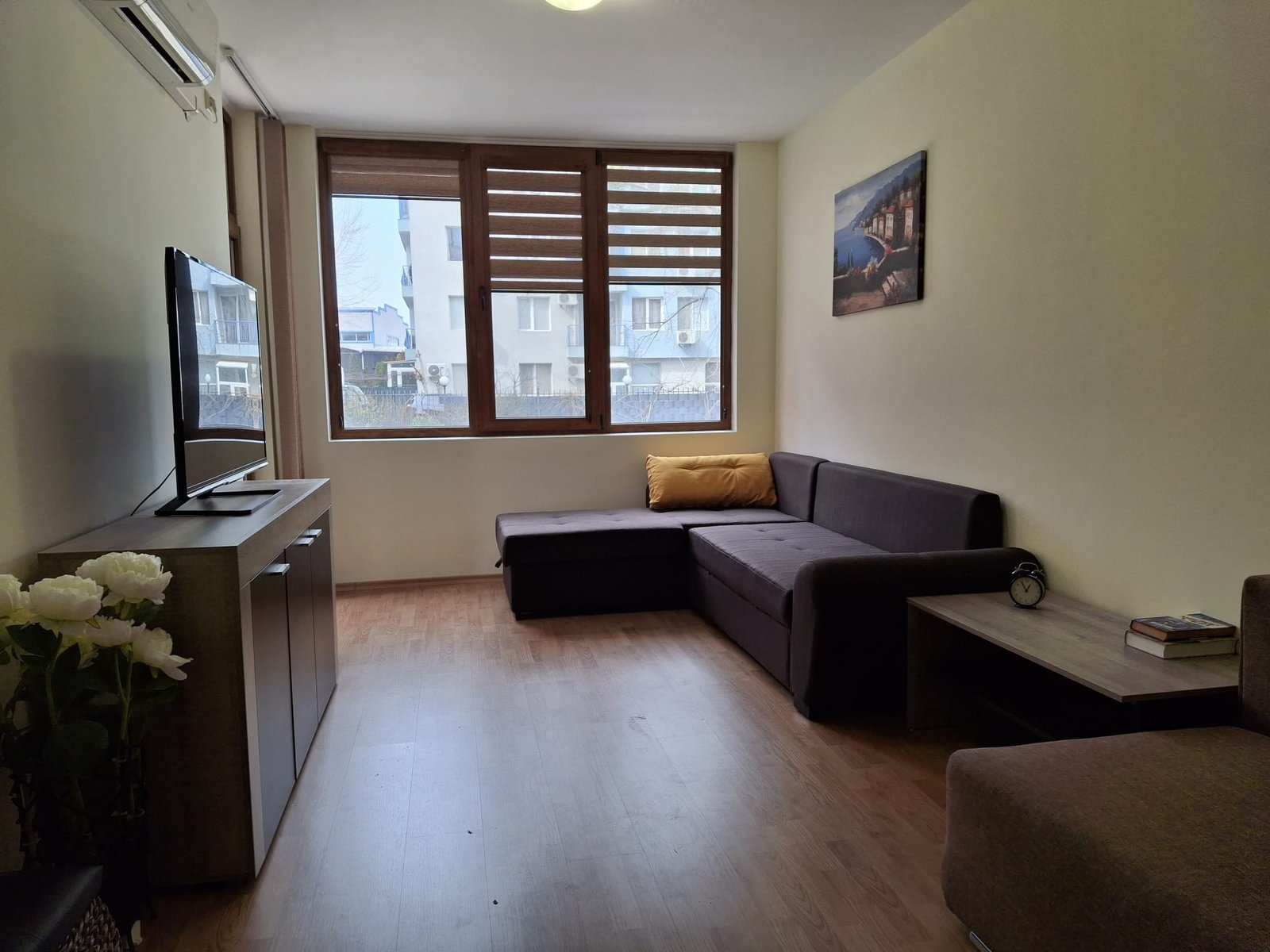 Современная гостиная с диваном, телевизором, столом и большим окном, оформленная в светлых тонах.