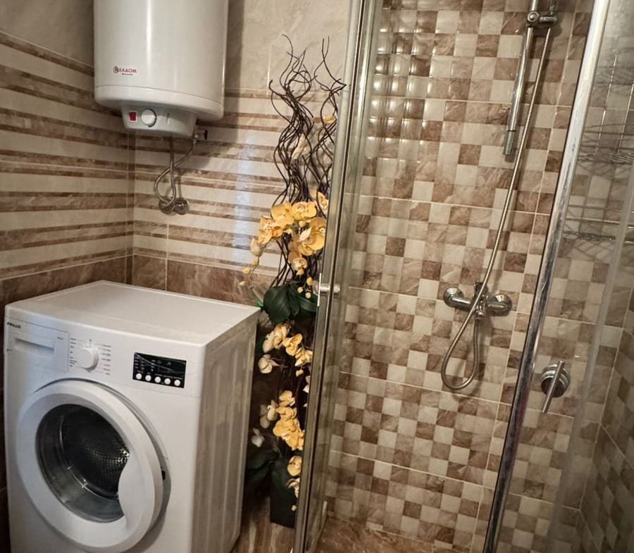 Современная ванная комната с душевой кабиной, стиральной машиной и декоративными элементами, идеальна для комфортной жизни в Болгарии.