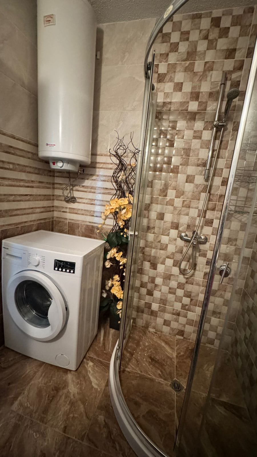 Современная ванная комната с душевой кабиной, стиральной машиной и декоративными элементами, идеальна для комфортной жизни в Болгарии.