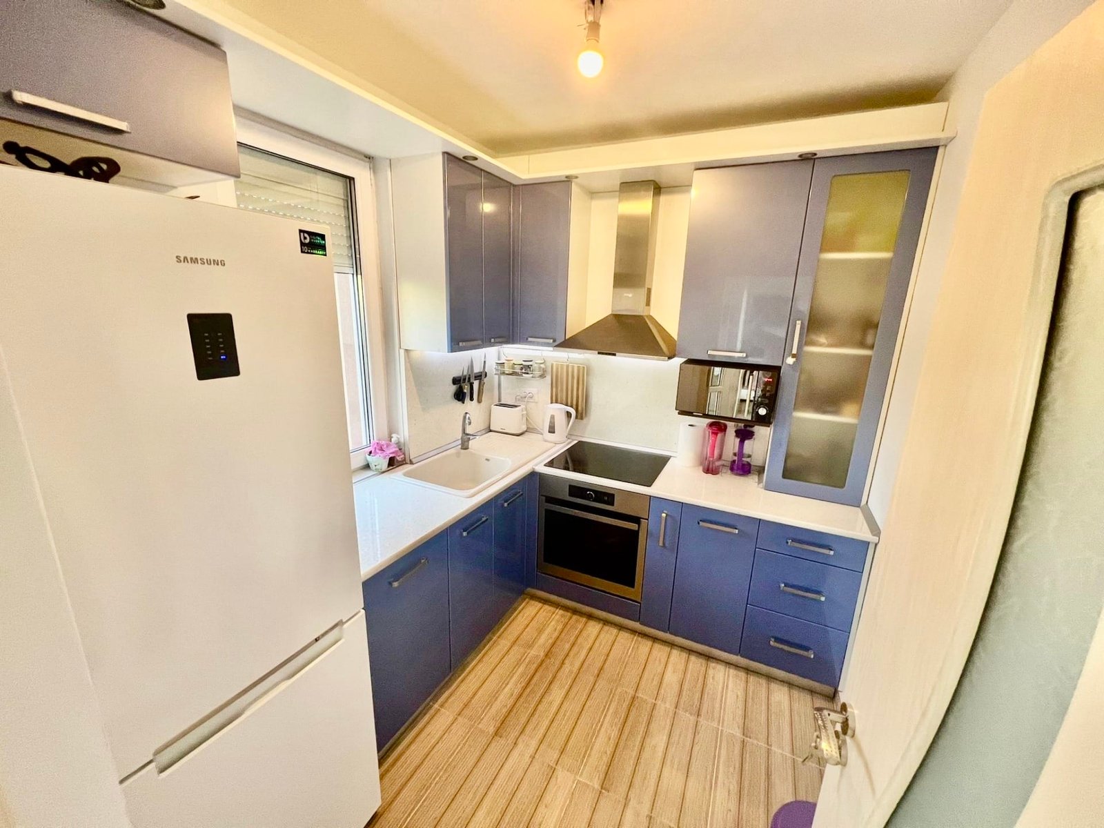 Современная кухня в болгарской квартире, сине-белый цвет мебели, техника, включая холодильник и варочную панель.