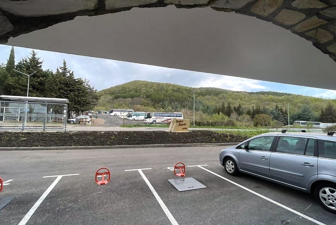 Парковка с серым автомобилем на переднем плане, гористый пейзаж на заднем фоне, место для отдыха и продажи недвижимости в Болгарии.