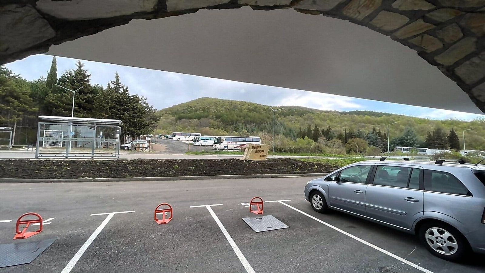 Парковка с серым автомобилем на переднем плане, гористый пейзаж на заднем фоне, место для отдыха и продажи недвижимости в Болгарии.