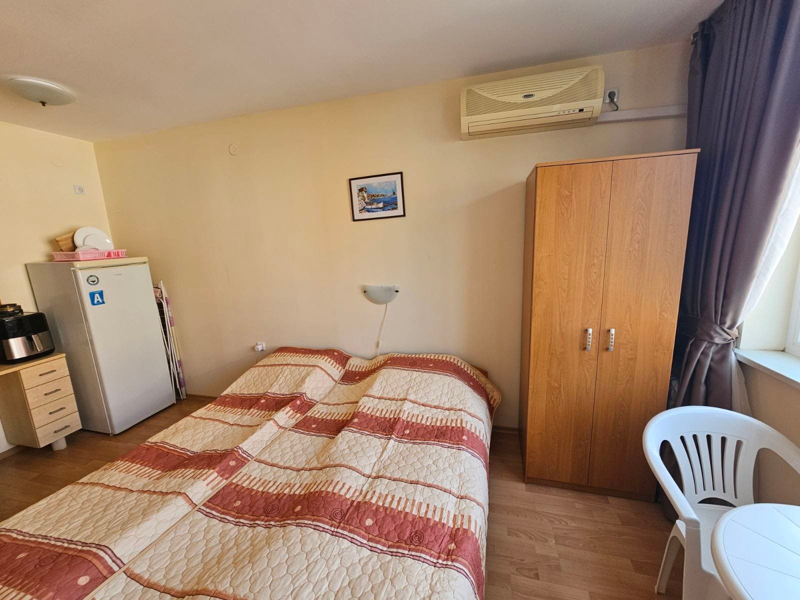 Уютный номер с двуспальной кроватью, шкафом, холодильником и светлым интерьером, идеальный для отдыха в Болгарии.