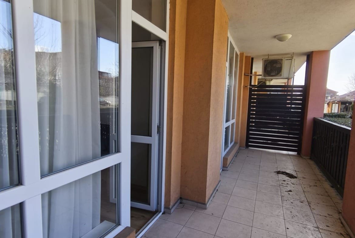 Балкон квартиры в Болгарии с панорамными окнами, плиточным полом и деревянной перголой, готовый для продажи или аренды.