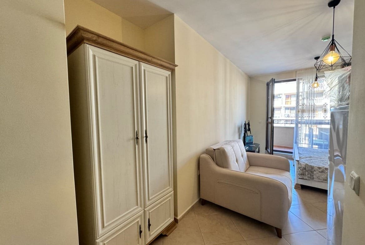 Светлая комната с диваном и шкафом, выход на балкон, идеальное предложение для покупки недвижимости в Болгарии.