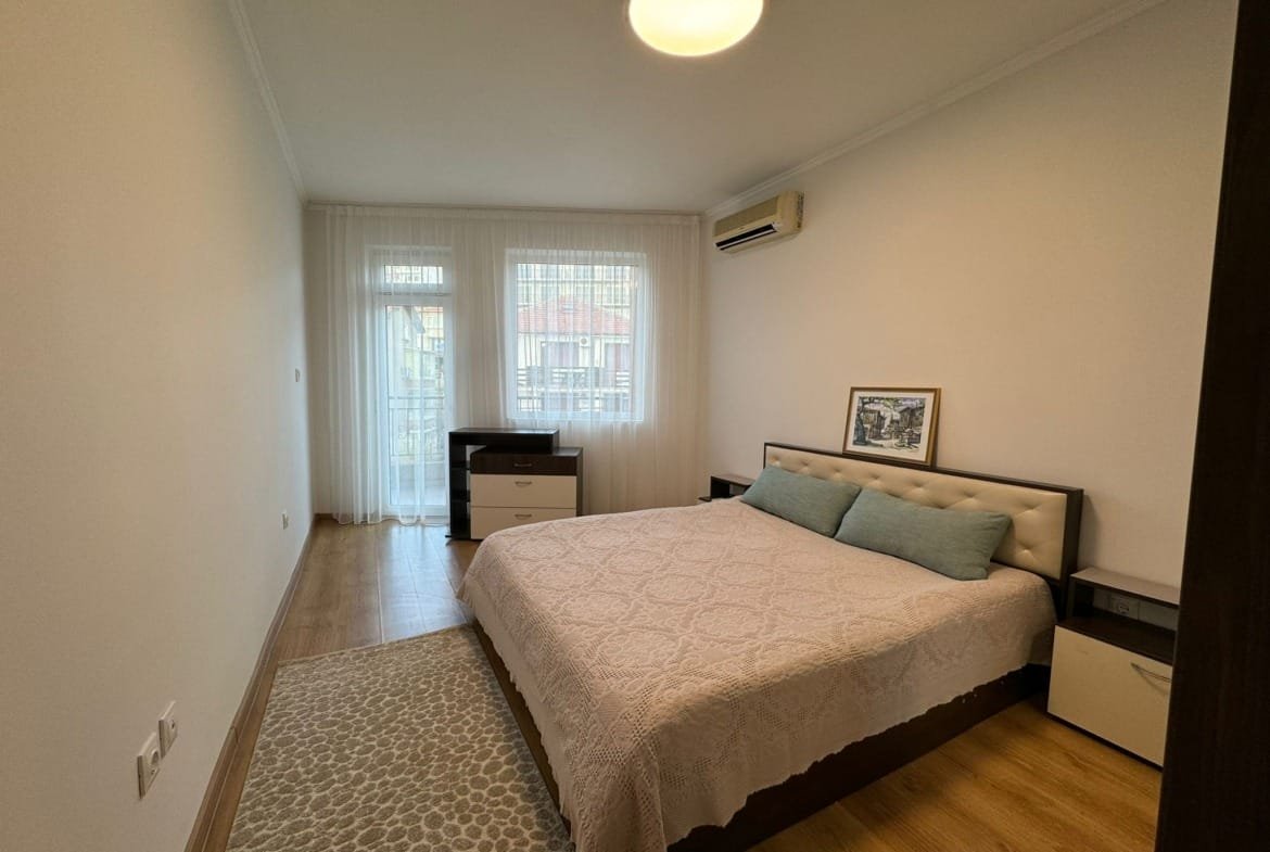 Современная спальня с двуспальной кроватью, комодом и светлым декором, идеально подходит для покупки недвижимости в Болгарии.