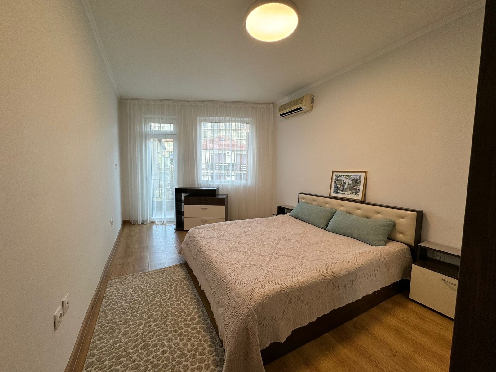 Современная спальня с кроватью и светлым интерьером. Современная спальня с двуспальной кроватью, комодом и светлым декором, идеально подходит для покупки недвижимости в Болгарии.