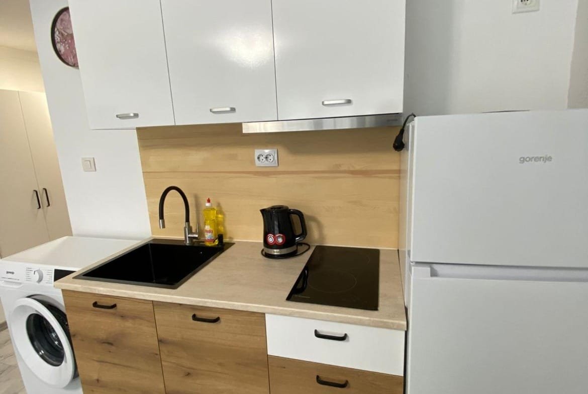 Современная кухня с белыми и деревянными фасадами, встроенной техникой и стиральной машиной, идеально для покупки недвижимости в Болгарии.