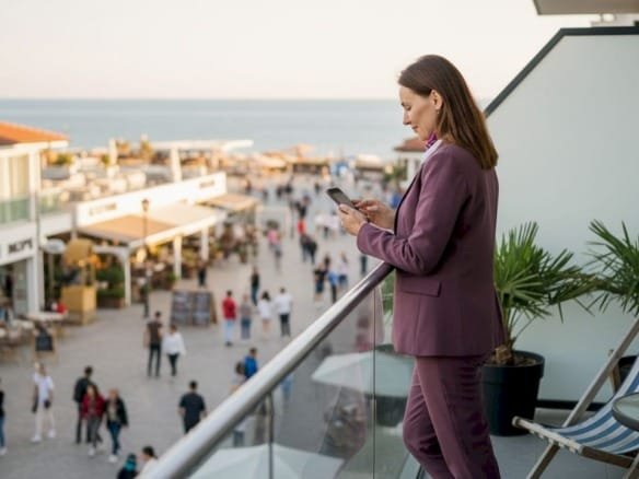 Инвестор стоит на балконе с видом на прибрежные кафе и магазины, оценивая перспективы бизнеса у моря.