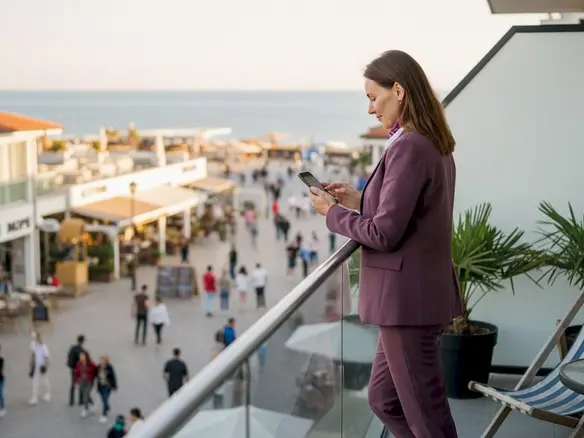 Инвестор стоит на балконе с видом на прибрежные кафе и магазины, оценивая перспективы бизнеса у моря.