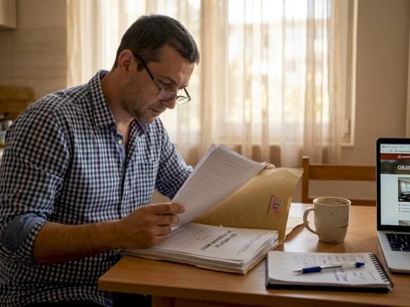 Мужчина внимательно изучает документы на квартиру прямо у себя дома.