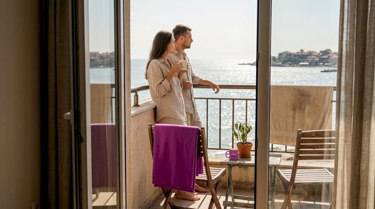 Пара наслаждается утренним кофе с видом на море в уютной квартире.