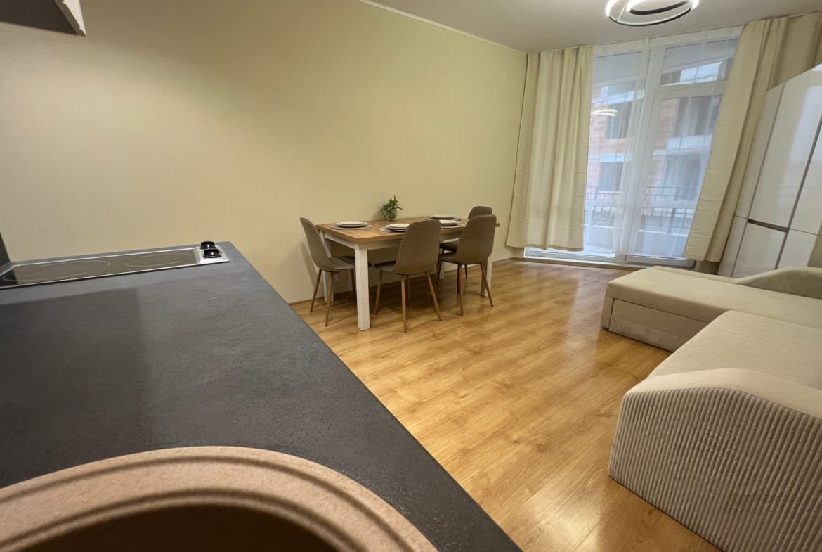 Современная гостиная с кухней, обеденным столом и мягкой мебелью, оформленная в светлых тонах, идеальна для жизни в Болгарии.