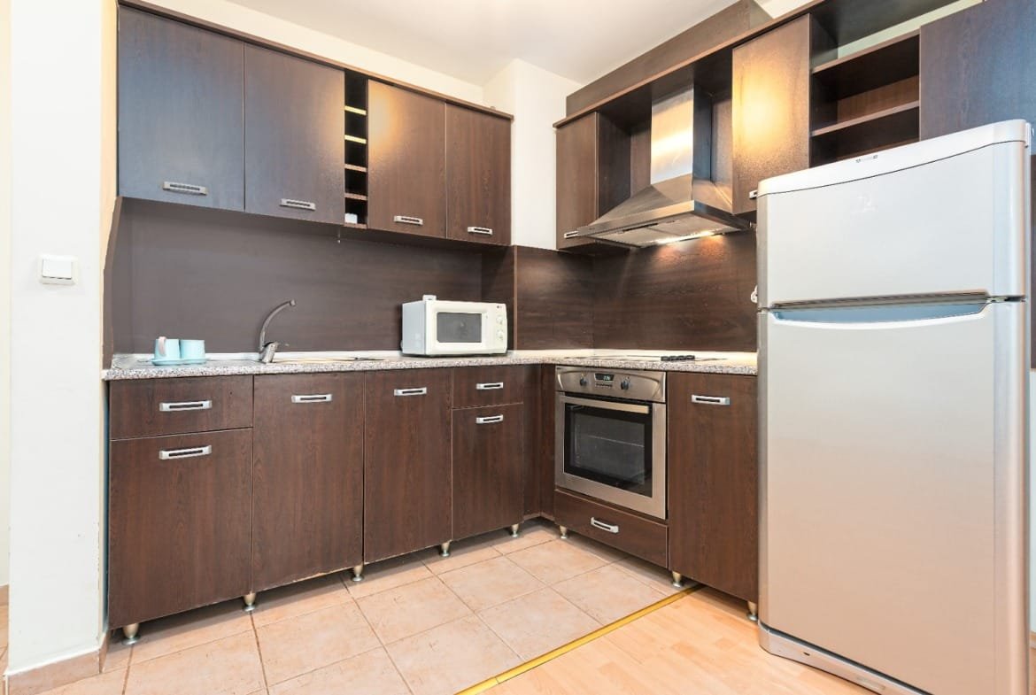 Современная кухня с деревянными шкафчиками, встроенной техникой и гранитной столешницей в недвижимости Болгарии.