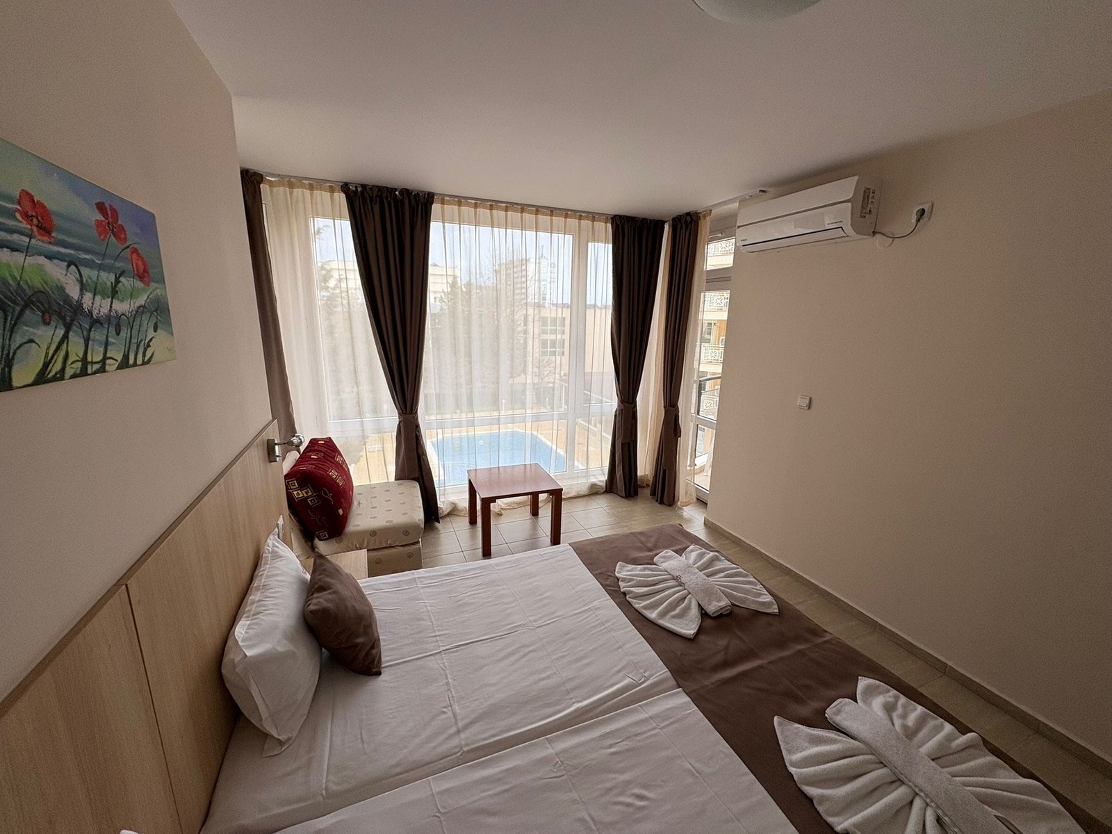 Современная спальня в Болгарии с двумя кроватями, видом на бассейн и яркими занавесками. Идеально для отдыха и продажи недвижимости.