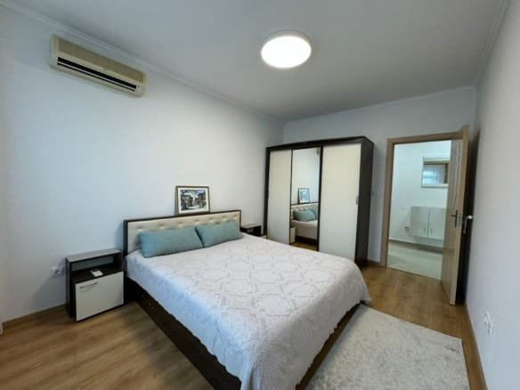 Современная спальня с двуспальной кроватью, шкафом, светлым интерьером и кондиционером, идеальная для покупки недвижимости в Болгарии.