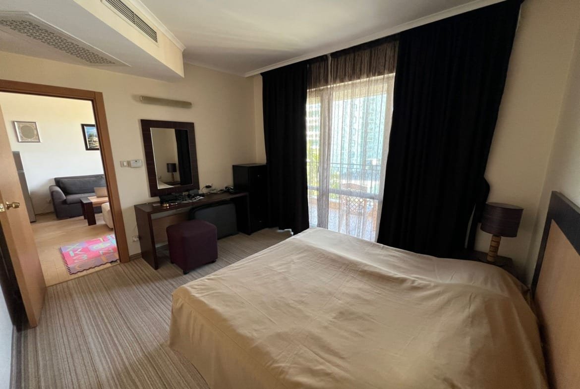 Уютный номер в гостинице Болгарии с двуспальной кроватью, письменным столом и балконом, освещённый естественным светом.