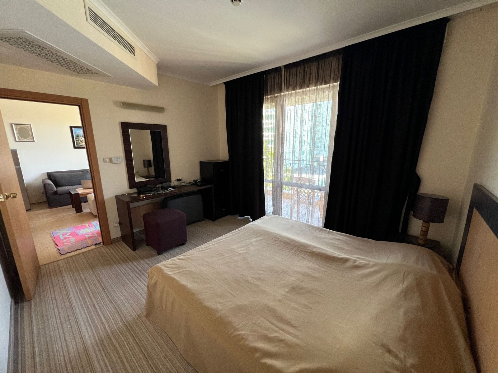 Уютный номер в отеле с балконом и современными удобствами Уютный номер в гостинице Болгарии с двуспальной кроватью, письменным столом и балконом, освещённый естественным светом.