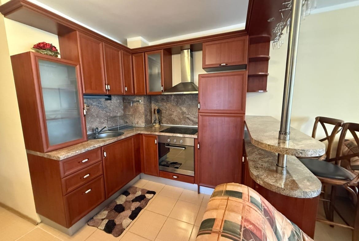 Современная кухня с деревянными шкафами, плитой и барной стойкой, идеально подходит для продажи квартир в Болгарии.