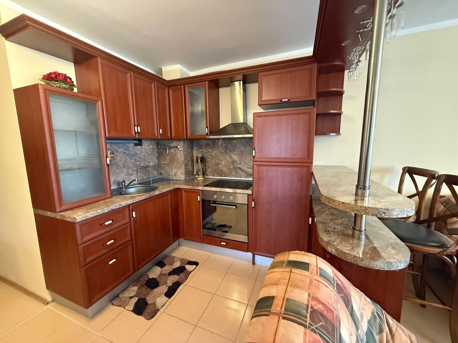 Современная кухня с деревянными шкафами, плитой и барной стойкой, идеально подходит для продажи квартир в Болгарии.