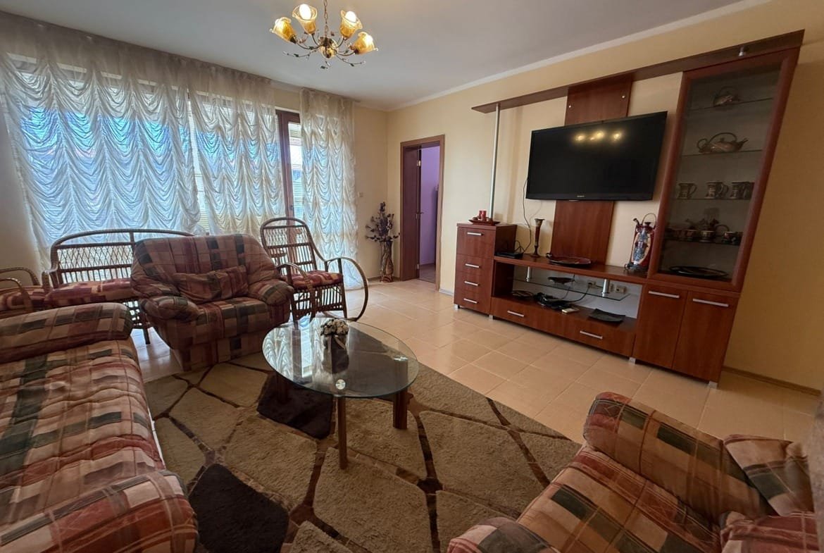 Современный интерьер гостиной с мягкой мебелью, телевизором и стеклянным столом, идеально подходящий для жилья в Болгарии.