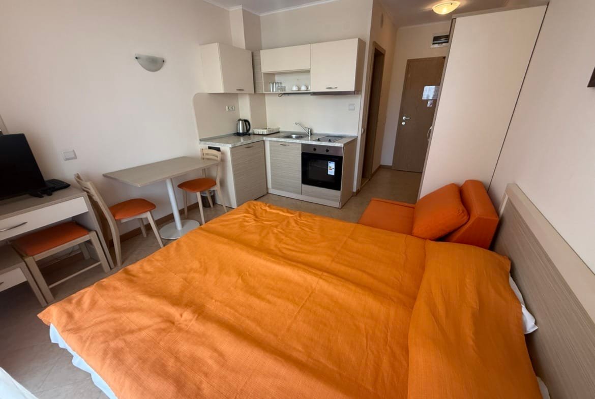 Светлая квартира в Болгарии с оранжевым текстилем, кухонным уголком и столовой зоной, идеально подходит для сдачи в аренду.