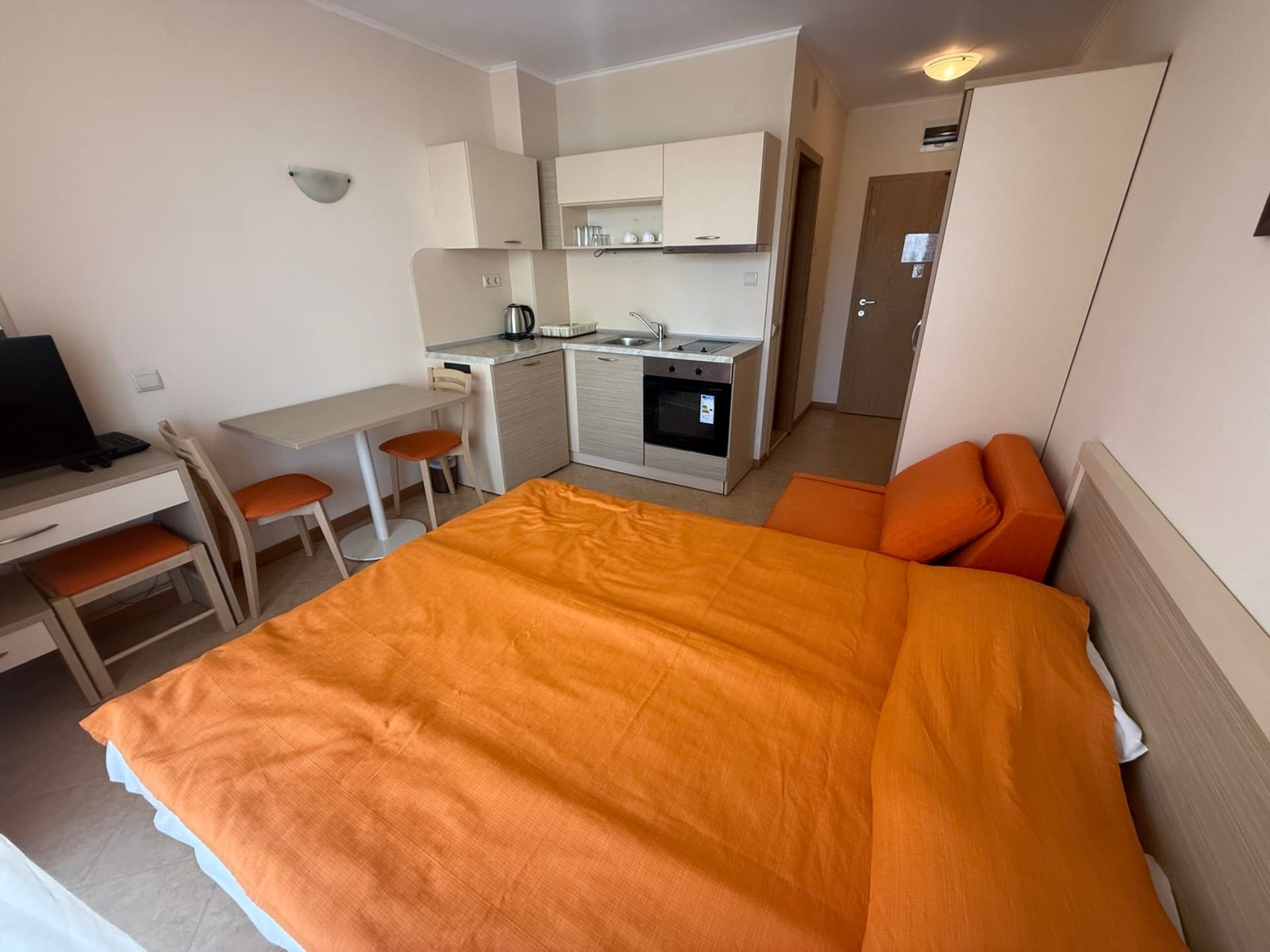 Светлая квартира в Болгарии с оранжевым текстилем, кухонным уголком и столовой зоной, идеально подходит для сдачи в аренду.