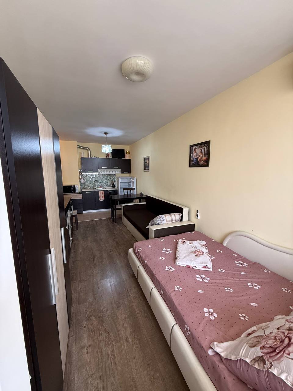 Однокомнатная студия с кухней, светлыми стенами и современной мебелью, окно с видом на улицу.