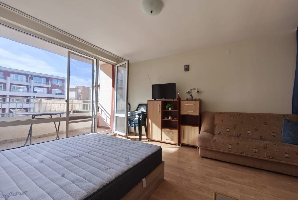 Современная квартира с балконом в Болгарии, светлая спальня и уютная мебель для комфортного проживания.