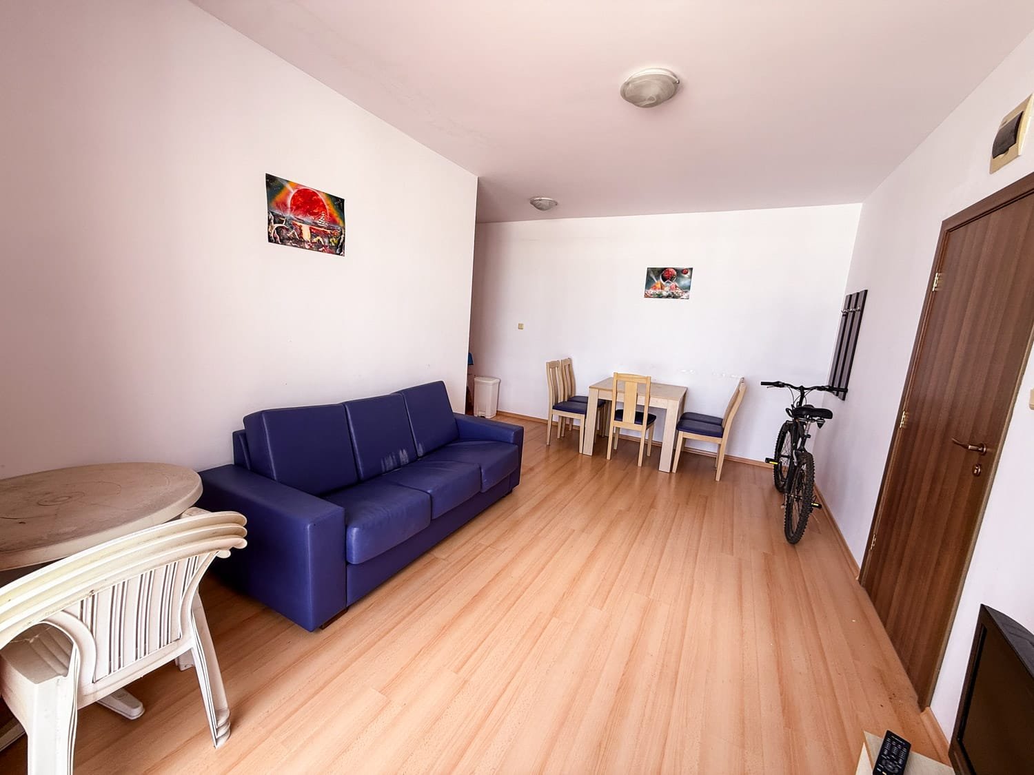 Современная квартира в Болгарии с удобной мебелью, столом, стульями и велосипедом в светлом интерьере.