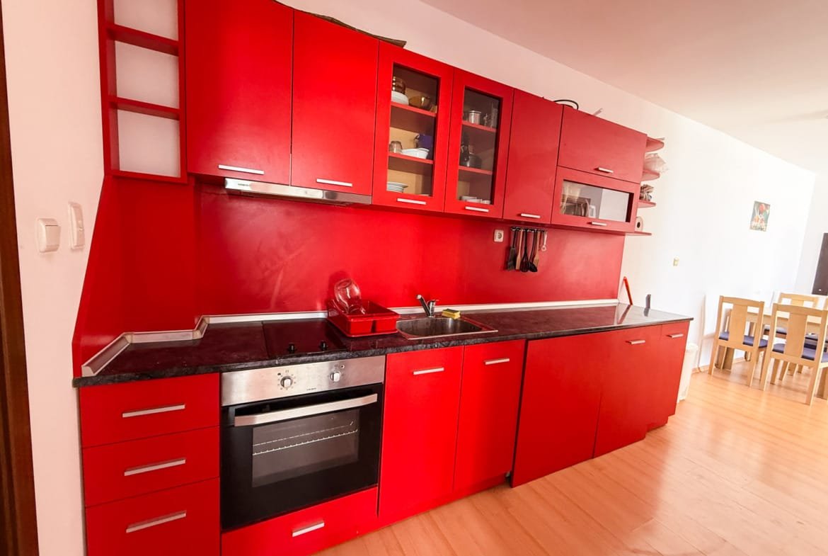 Яркая кухня с красными шкафами и черной столешницей, идеально подходит для покупки недвижимости в Болгарии.