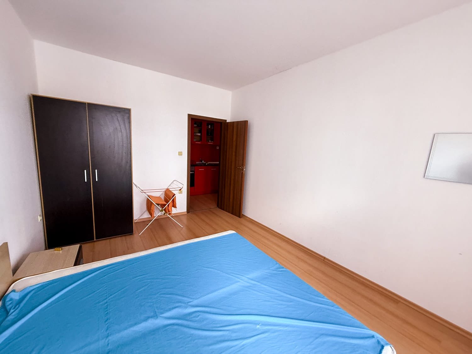 Современная спальня с односпальной кроватью, шкафом и кухней на фоне, идеально подходит для покупки недвижимости в Болгарии.