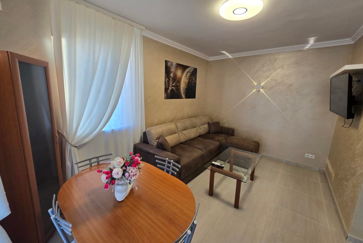 Современный интерьер уютной квартиры в Болгарии с диваном, столом и телевизором, идеально подходит для комфортного проживания.