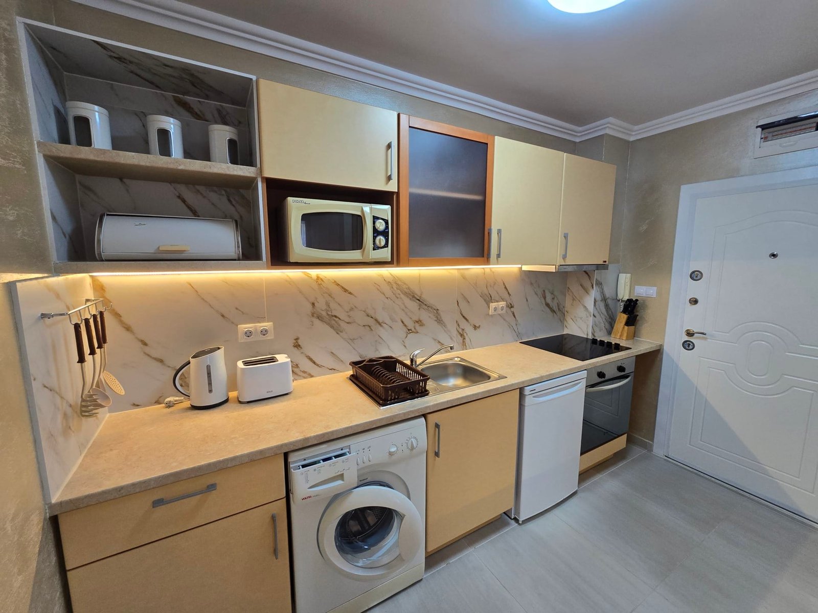 Современная кухня с встроенной техникой, стиральной машиной и плитой, оформленная в светлых тонах, для продажи недвижимости в Болгарии.